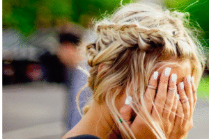 Female with blond braided hair covering face with hands.